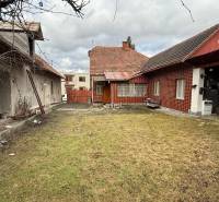 The courtyard of a family house in Babiná with two buildings and a grassy area.