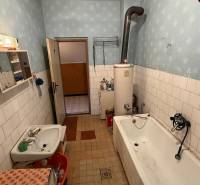 The bathroom in the family house contains a bathtub, a sink, old furniture, and a boiler.