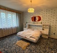 A bedroom in a family house with a floral carpet and a large window.