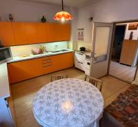 A kitchen in a family house with an orange kitchen unit, table, and a wooden decor floor.