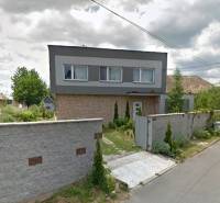 A family house in Bystrička with a landscaped garden and a high fence along the street.