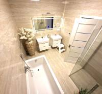Bathroom in a family house with a bathtub, sink, floral arrangement, and large mirror.