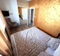 A bedroom in a family house with a wood-patterned floor, brown curtains, and a patterned bed.
