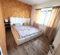 Bedroom in a family house with a bed, wood-patterned floor, and a golden wall.
