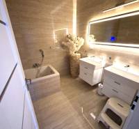 A bathroom in a family house with a bathtub, mirror, and cabinets. Floor with wood decor.