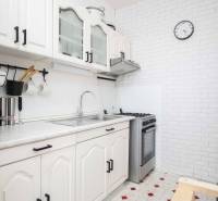 A kitchen in a 3-room apartment with white furniture and a wall clock.