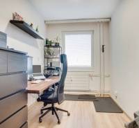Home office with a desk, chair, and shelf in a 3-room apartment with wood-patterned flooring.
