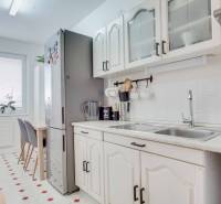 A kitchen in a 3-room apartment with white cabinets, a dining table, and a large refrigerator.