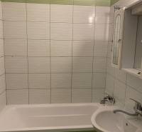 A bathroom in a 3-room apartment with green tiles and a bathtub next to the sink.