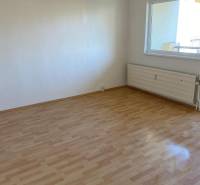 A room with a wooden decor floor in a 3-room apartment, light wall, radiator.