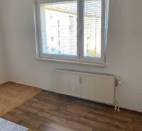 White wall, window with blinds, floor with wood decor, radiator in a 3-room apartment.