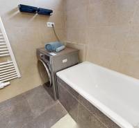 A bathroom in a 3-room apartment with a bathtub, a washing machine, and towels on beige tiles.