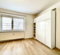 A room with a large window, a wardrobe, and a floor with a wooden decor in a studio apartment.