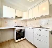 A kitchen in a studio apartment with white cabinets and a wooden decor floor.