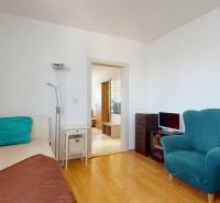 A room in a 4-room apartment with a sofa, a bed, and a floor with a wooden decor.