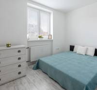 A bright bedroom with a double bed, a dresser, and a wooden decor floor in a two-room apartment.