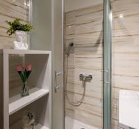 Bathroom with an enclosed shower, a shelf with decorations, and a washing machine in a 2-room apartment.