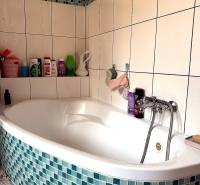 A bathroom with a corner bathtub and blue-white tiles in a 2-room apartment.