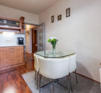 A kitchen in a 4-room apartment with a glass table, wooden decor flooring, white walls.