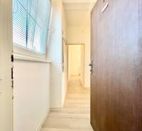 A hallway with a wooden decor floor, white walls, a large window with blinds.