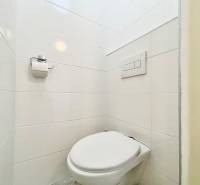 A toilet with white tiles and toilet paper in a studio apartment.