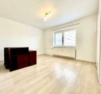 A room with a wooden decor floor and simple furniture in a studio apartment.