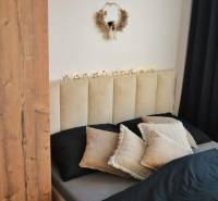 Bedroom in a 3-room apartment with a decorative wreath and black curtains; bed with pillows.