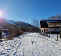 A snowy road in front of the cottage on the street in Mýto pod Ďumbierom, on a sunny winter day.