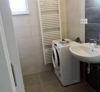 A small bathroom contains a washing machine, a sink, and a radiator, on Bodona Street in a studio apartment.