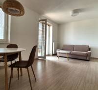 A studio apartment on Bodona Street with wooden furniture, a sofa, a table, a balcony, and a kitchenette.