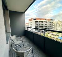 Balcony with two chairs and wood-patterned tiles, view of buildings.