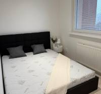 Bedroom in a 2-room apartment with a black headboard, white bedspread, and window with blinds.