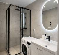 Bathroom in a 2-room apartment with a washing machine, shower cabin, and illuminated mirror.