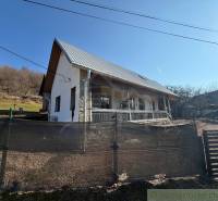A family house in Ratkovské Bystré with a sloped plot, a metal roof, and a wooden fence.