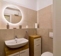 Compact bathroom in a studio apartment with a sink, illuminated mirror, and light-colored tiles.