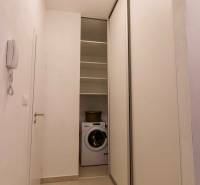 A narrow hallway in a one-room apartment with a washing machine and sliding doors.