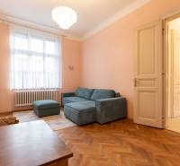 A bright living room with a sofa, chandelier, and wood-patterned flooring in a three-room apartment.