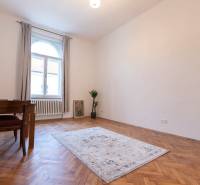 A room in a 3-room apartment with a wooden decor floor, a carpet, and a table.