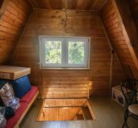 The attic of the cottage with a window, a floor with a wooden decor, boxes, and a chair.