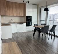 A kitchen with built-in appliances and a dining table in a 3-room apartment, floor with a wooden decor.