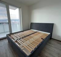 In the 3-room apartment, there is a bed with gray upholstery and a floor with a wooden decor.