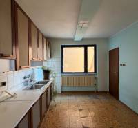 A kitchen in a family house with light blue walls and a window, and a floor with a wooden decor.