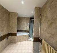 A bathroom in a family house with marble-look tiles and a corner bathtub.