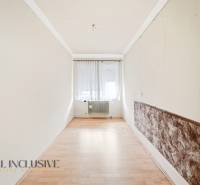 A narrow room with a wood-patterned floor, a window with curtains, a radiator.