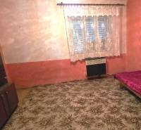 A room in a family house with a carpet, a bed, and a cabinet, with a curtain on the window.