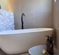 A bathroom in a family house with a bathtub, a stone-clad wall, and decorative bottles.