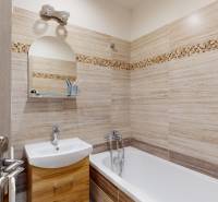Bathroom in a two-room apartment with light tiles and a bathtub, cabinets under the sink.