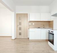 A kitchen in a 2-room apartment with white cabinets, a stove, and a wooden decor floor.