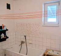 A bathroom in a family house with a bathtub, a shelf, and white tiles.