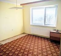 A room in a family house with a carpet, yellow walls, a table, and a ceiling light.